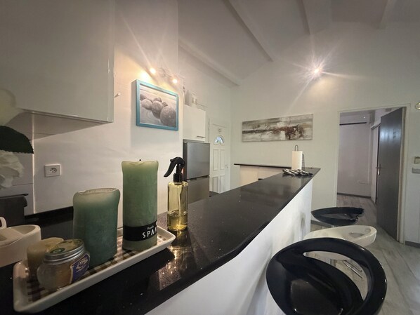A modern kitchen with a black countertop, a green candle, a spray bottle, and a jar of jam. - Right on the Water | Pool | Le Calme — Althéa (Le Gosier)