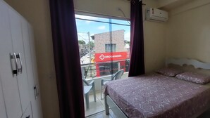Un dormitorio con una cama, una ventana con cortinas, un equipo de aire acondicionado y vista a un edificio con un letrero.