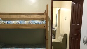 Una habitación con una cama litera y una cama individual, ambas con ropa de cama estampada con motivos florales. Se observa una puerta que da a otra habitación con una silla y una mesa.