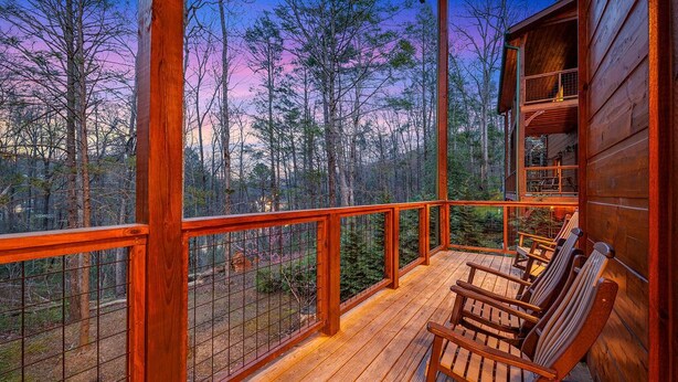 A wooden deck with chairs, a railing, and a view of a forested area. - Free Tickets | Theater, Game Room, Hot Tub, & Fire Pit, 1.5 Miles to Downtown (Gatlinburg)