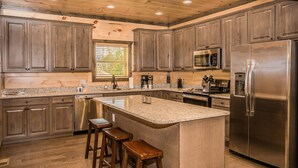 A modern kitchen with wooden cabinets, stainless steel appliances, and a granite countertop. - Free Tickets | Theater, Game Room, Hot Tub, & Fire Pit, 1.5 Miles to Downtown (Gatlinburg)