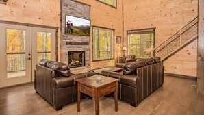 A spacious living room with a fireplace, leather sofas, and a TV mounted on the wall. - Free Tickets | Theater, Game Room, Hot Tub, & Fire Pit, 1.5 Miles to Downtown (Gatlinburg)