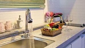 A kitchen sink with a modern faucet, a fruit basket, a wine glass, and a bottle of wine on the counter. - Boryeong Laon Pension (Boryeong)