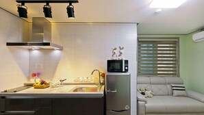A compact kitchen with a microwave, refrigerator, and a sink. There's a small seating area with a sofa and teddy bears. - Boryeong Laon Pension (Boryeong)