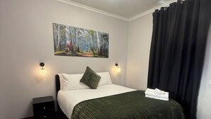 A bedroom with a bed, a nightstand, a wall-mounted painting, and a ceiling light fixture. - Deniliquin Pioneer Tourist Park (Deniliquin)
