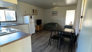 A compact kitchen with a stove, refrigerator, and a dining area with chairs and a table. - Deniliquin Pioneer Tourist Park (Deniliquin)