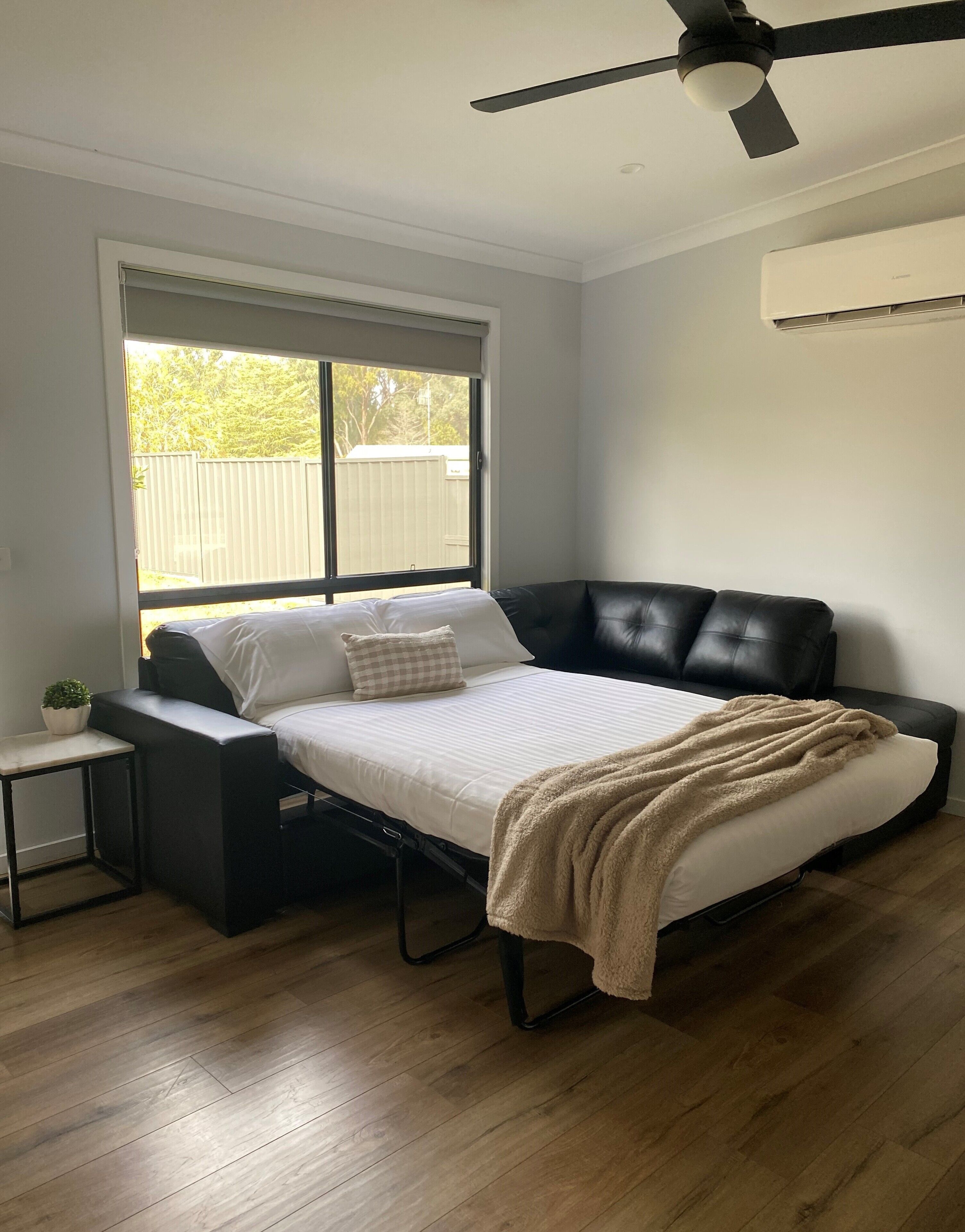 A bedroom with a bed, a small bedside table, a window, and a ceiling fan.