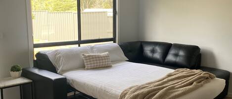A bedroom with a bed, a small bedside table, a window, and a ceiling fan.