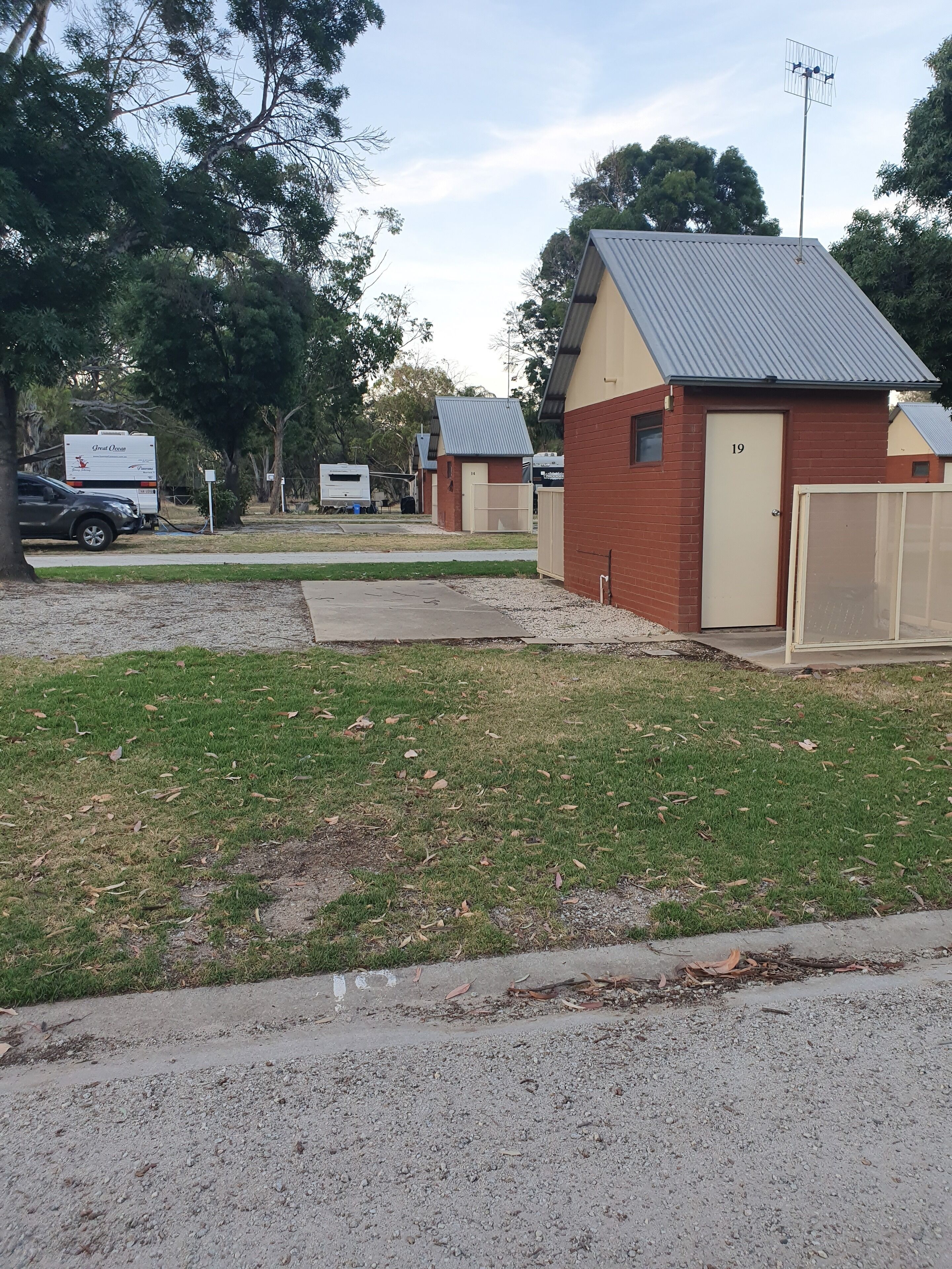 Un barrio residencial con un pequeño edificio de ladrillo número 19, un estacionamiento con portón y una caravana con el rótulo 'Great Ocean'.