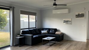 A modern living room with a black leather sofa, a small side table, and a wooden floor. - Deniliquin Pioneer Tourist Park (Deniliquin)