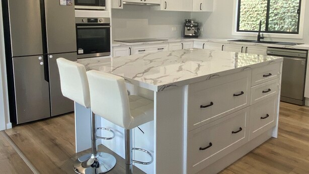 A modern kitchen with white cabinetry, a large island with bar stools, stainless steel appliances, and a window with a textured view. - Deniliquin Pioneer Tourist Park (Deniliquin)