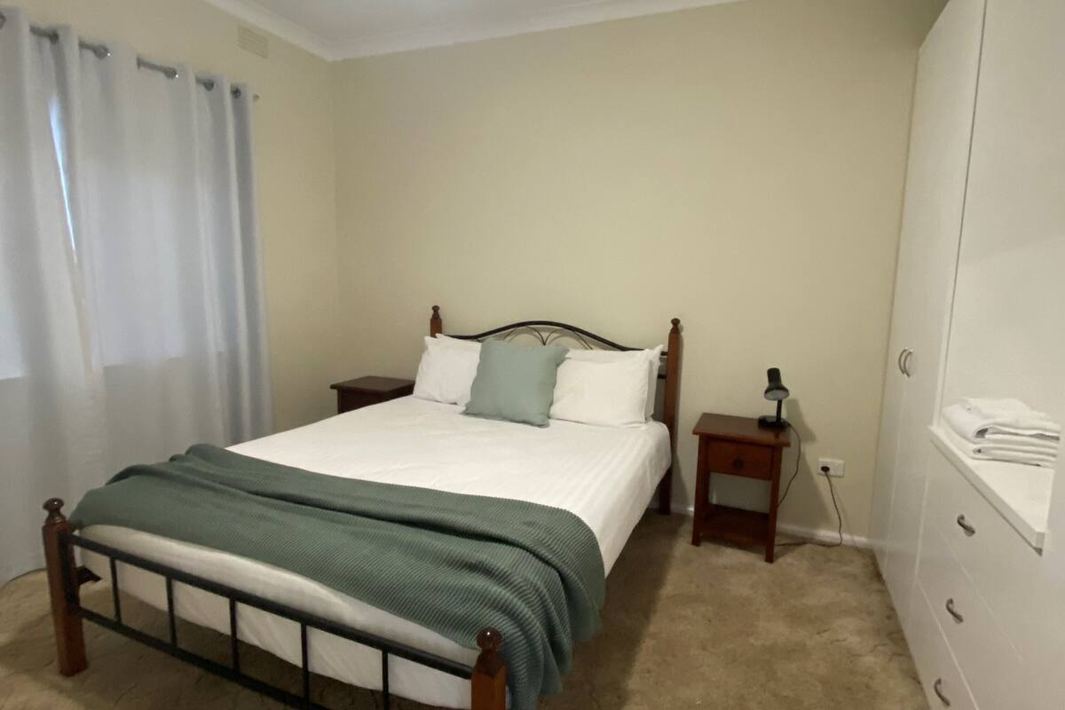 Ein Schlafzimmer mit Bett, Nachttisch, Lampe und Kleiderschrank.