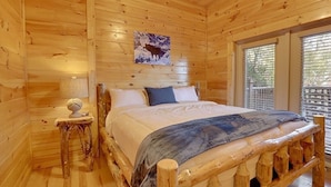 Ein Zimmer in einer Holzhütte mit einem Bett, einem kleinen Tisch und einem Fenster.