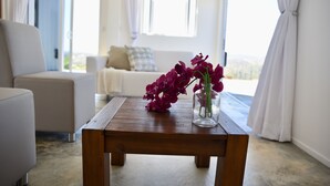 A wooden table with a vase of purple flowers in a room with a white sofa and a view through a window. - FonteinTop - 360° Panoramic View (Willemstad)