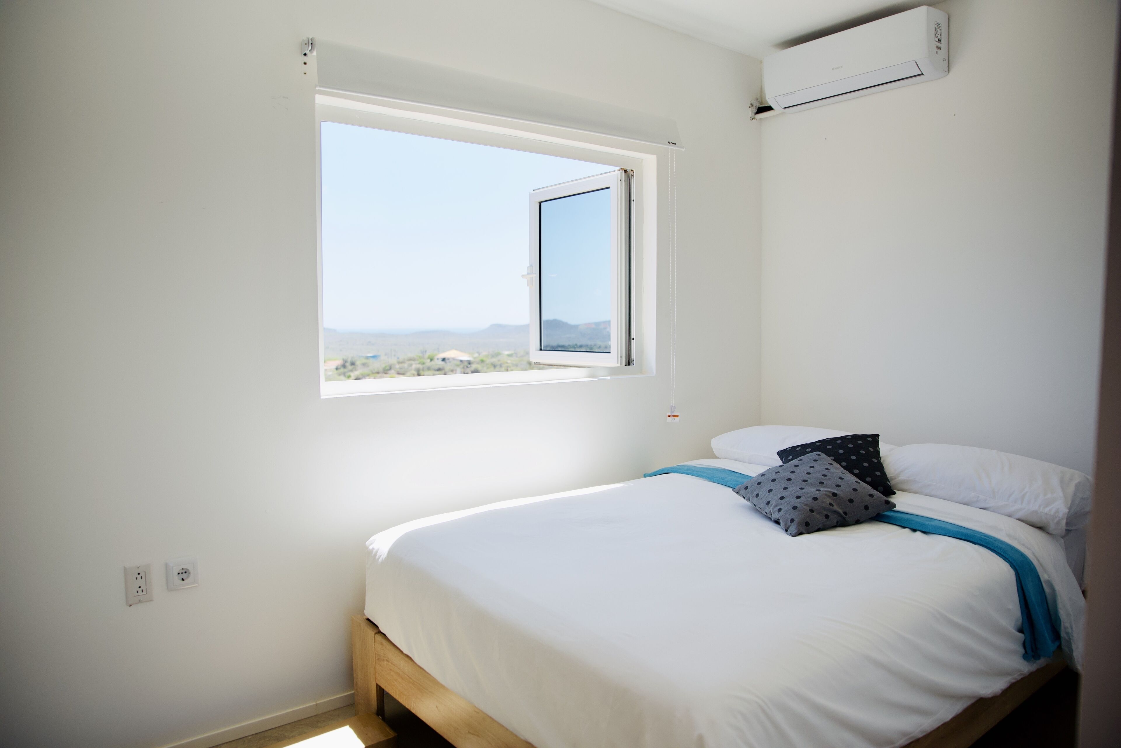 A bedroom with a single bed, a window with an open shutter, and an air conditioning unit on the wall.