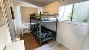 Pieni, kompakti huone, jossa on kerrossängyt, valkoinen tuoli ja ikkuna, josta tulee luonnonvaloa.