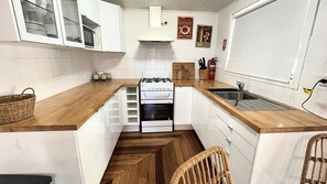 Kompakti keittiö, jossa on valkoiset kaapit, kaasuliesi, sisäänrakennettu uuni ja puinen työtaso.