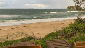 A beach with waves, a sandy shore, and wooden benches.