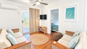Uma sala de estar com sofá, televisão, estante de livros e um quadro na parede.