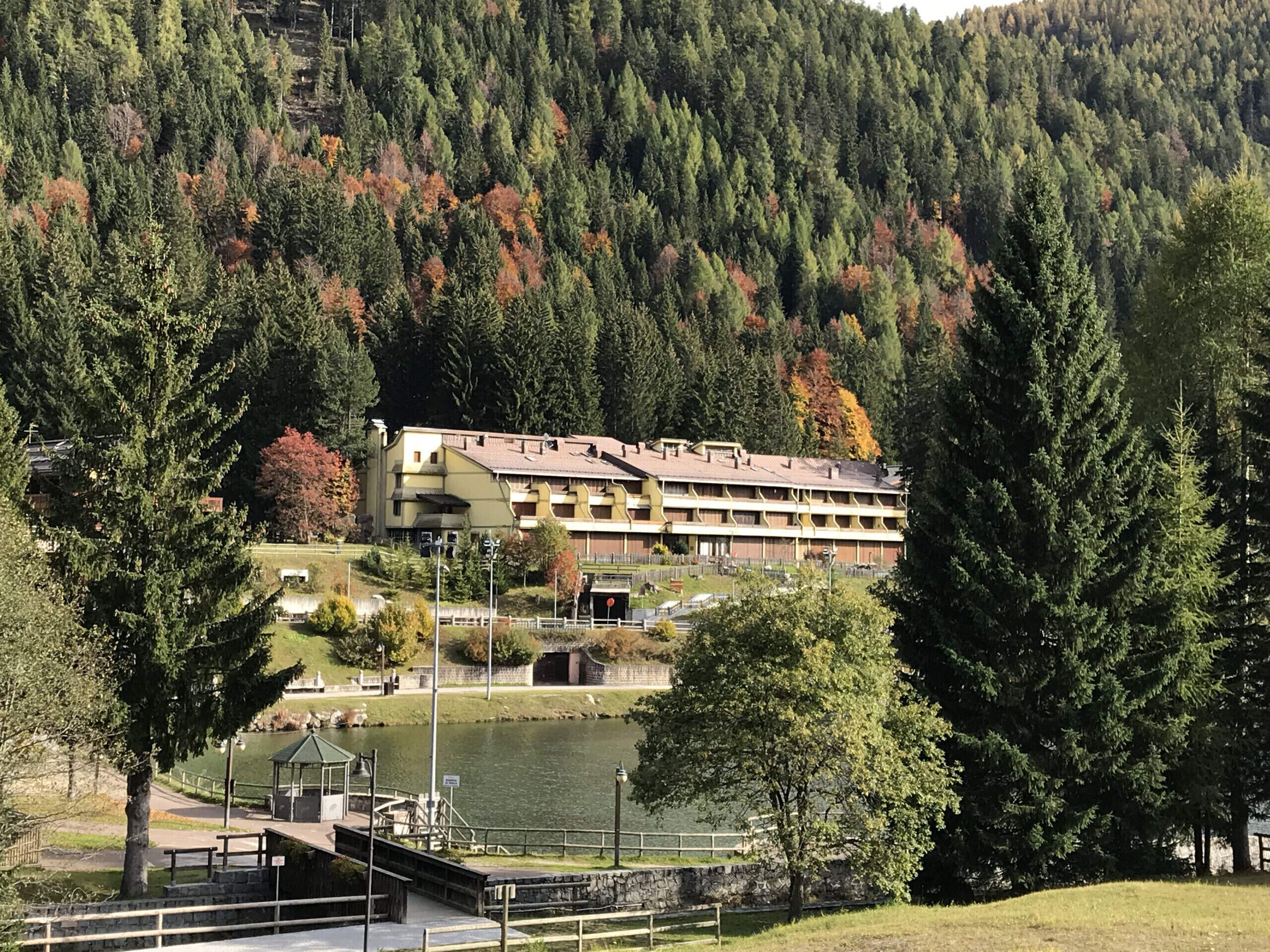 A hotel with a multi-story structure, a parking area, and a lake in the foreground.