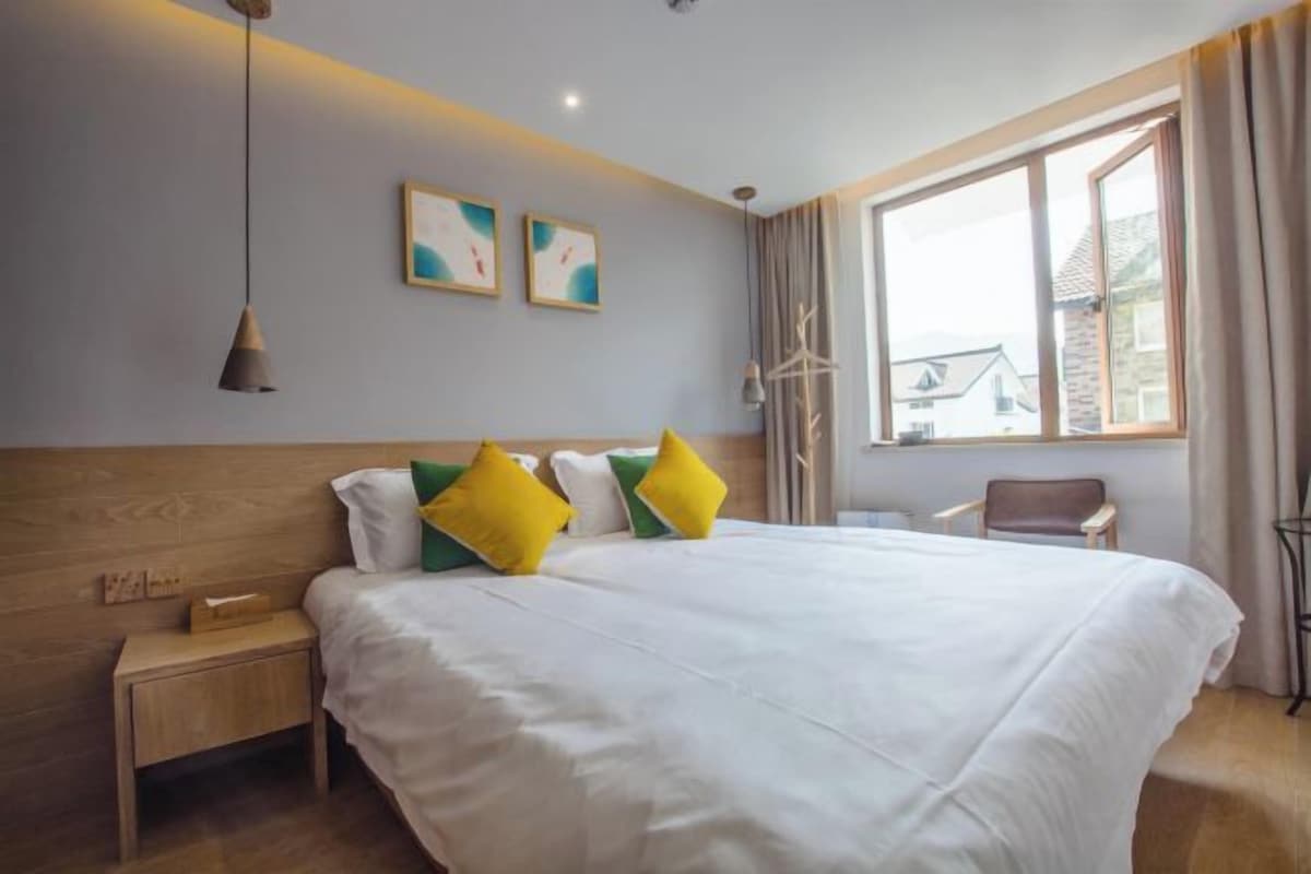A hotel room with a large bed, bedside tables, a window with curtains, and artwork on the wall.