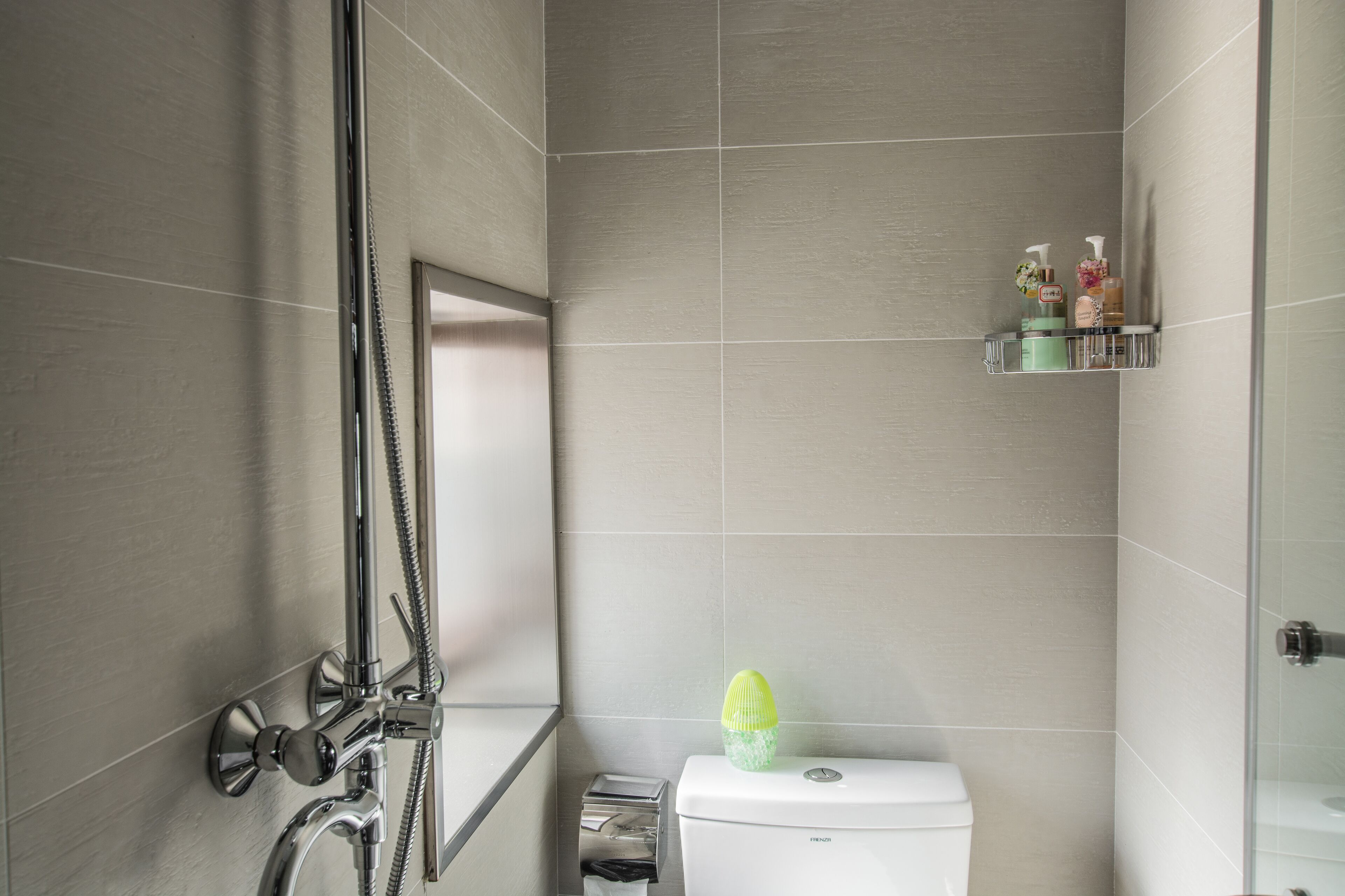 A modern bathroom with a shower, toilet, and a shelf with toiletries.