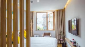 Une chambre d’hôtel avec un lit, une chaise, une télévision et une fenêtre donnant sur des immeubles.