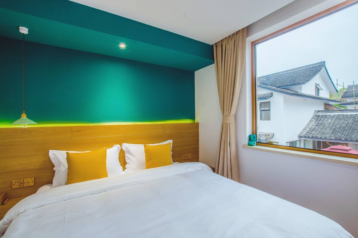 Een slaapkamer met een bed, een raam met uitzicht op gebouwen en een groene wand.