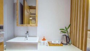 Une salle de bain avec un lavabo blanc, un miroir, un meuble en bois, une plante et un plateau contenant des articles de toilette.