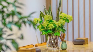 Une table à manger ornée d’un vase de fleurs vertes, une chaise en bois et un petit pot vert contenant une cuillère en bois.