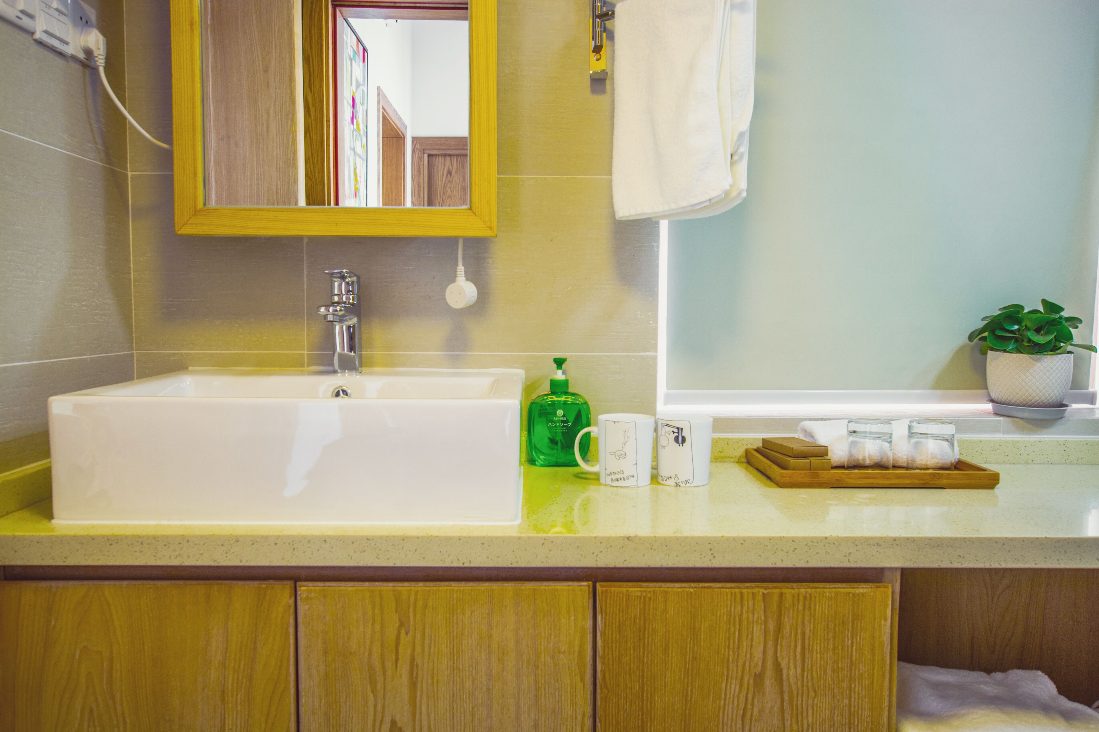 A bathroom with a white sink, a mirror, a towel, a green bottle, and a tray with towels.