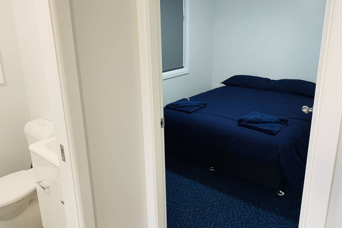 A small, clean room with a bed, a window, and a toilet.