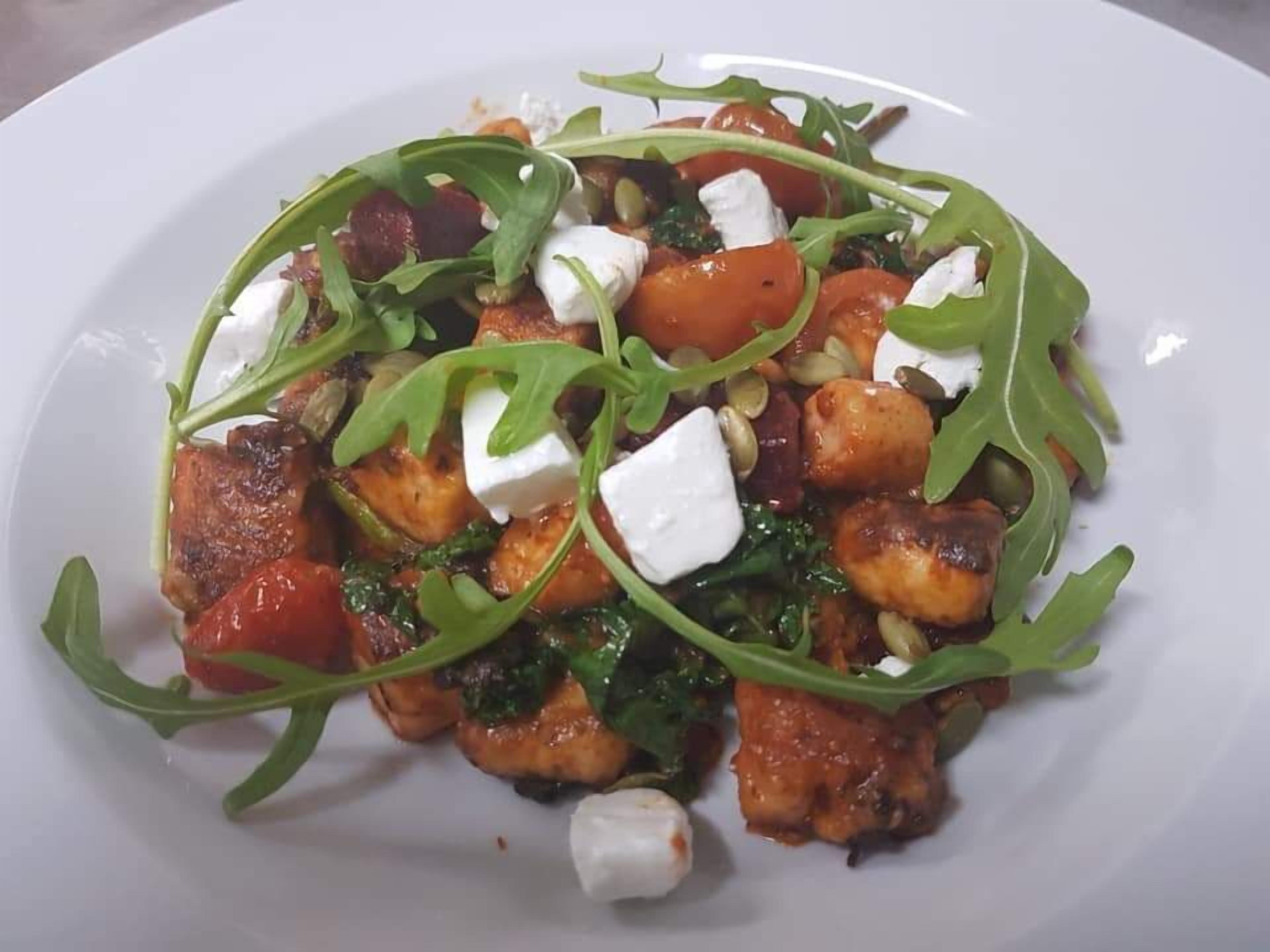 A plate of food with arugula, tomatoes, cheese, and possibly meat or tofu.