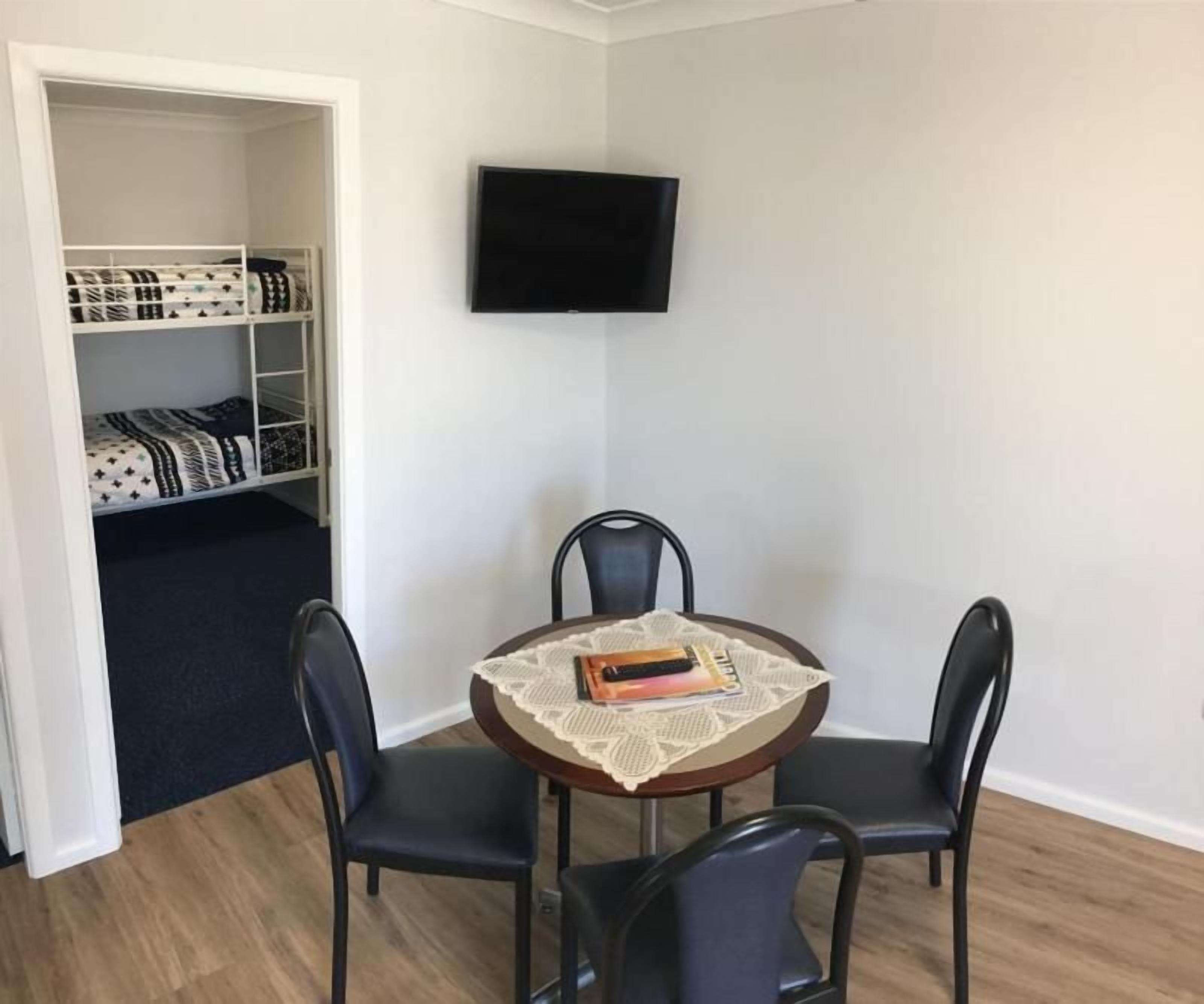 A room with a bunk bed, a round table with four chairs, and a flat-screen TV mounted on the wall.