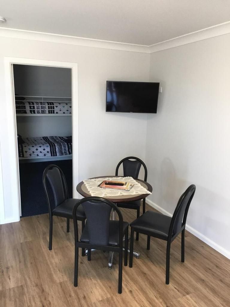 Una habitación con una mesa de comedor y sillas, un televisor montado en la pared y un armario con ropa de cama estampada.