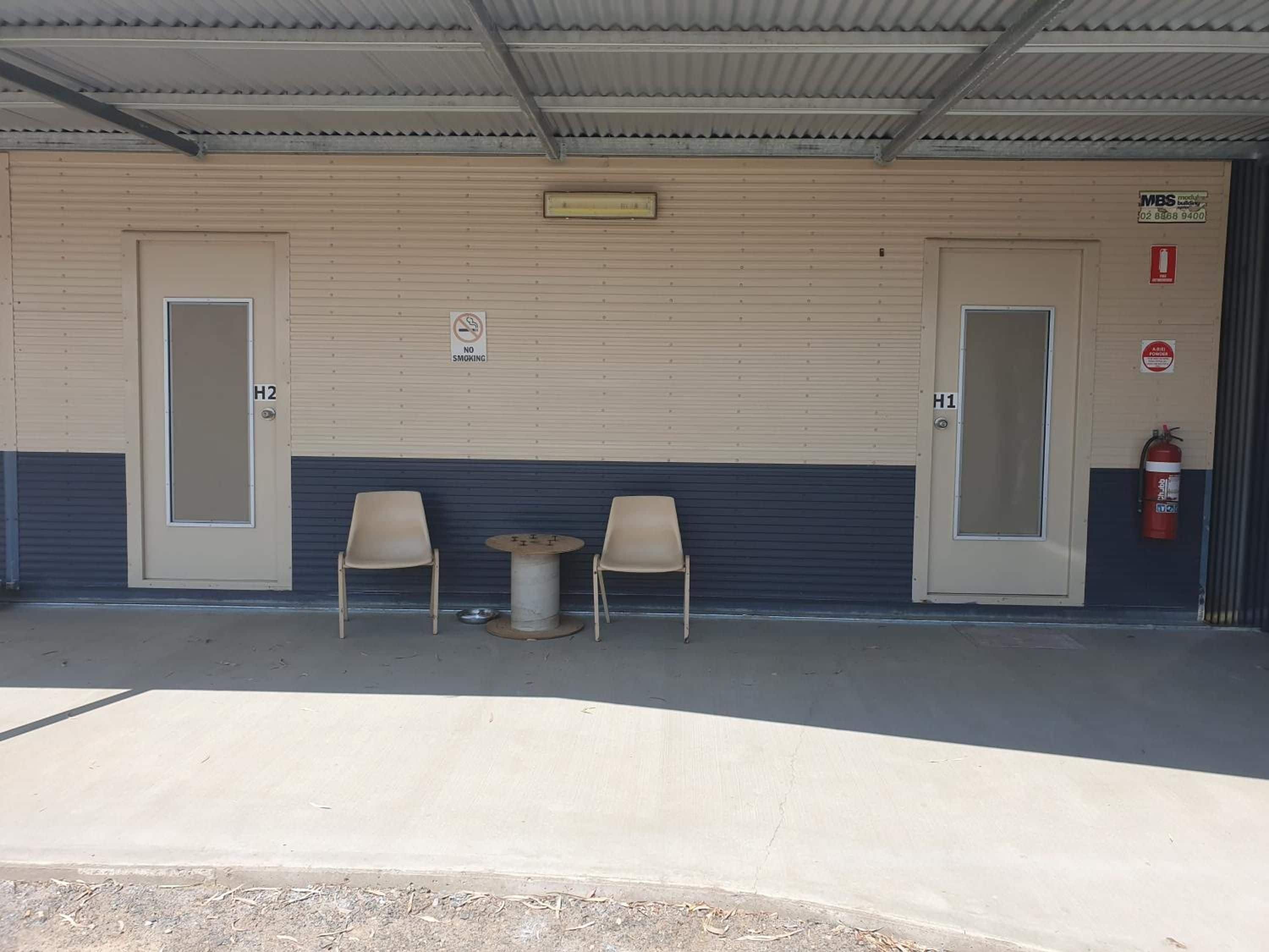 A covered outdoor area with two doors marked H2 and H1, a no-smoking sign, and a fire extinguisher.