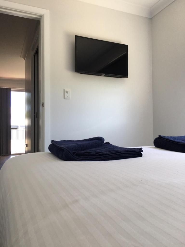A hotel room with a bed, a flat-screen TV mounted on the wall, and a neatly folded towel on the bed.