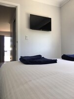 Habitación de hotel con cama, televisor de pantalla plana montado en la pared y una toalla doblada con cuidado sobre la cama.