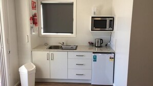 Una cocina compacta equipada con microondas, lavamanos y un refrigerador pequeño.