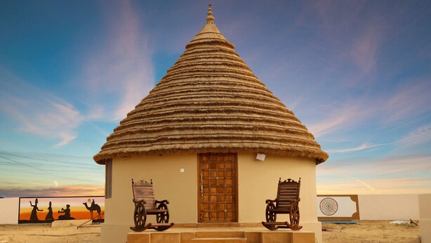 Un petit bâtiment à toit de chaume, doté d’une porte en bois et d’un escalier menant à l’entrée.