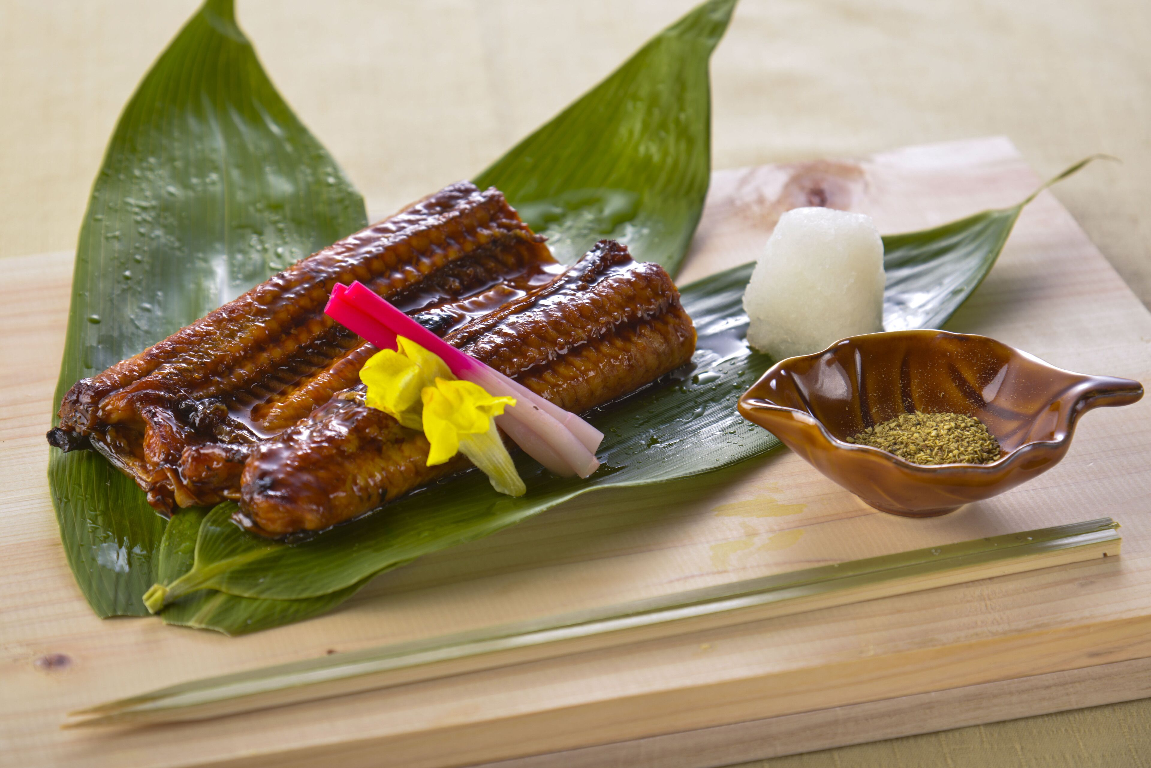 A traditional dish with rice cakes, a small bowl of seasoning, and a decorative flower on a leaf.