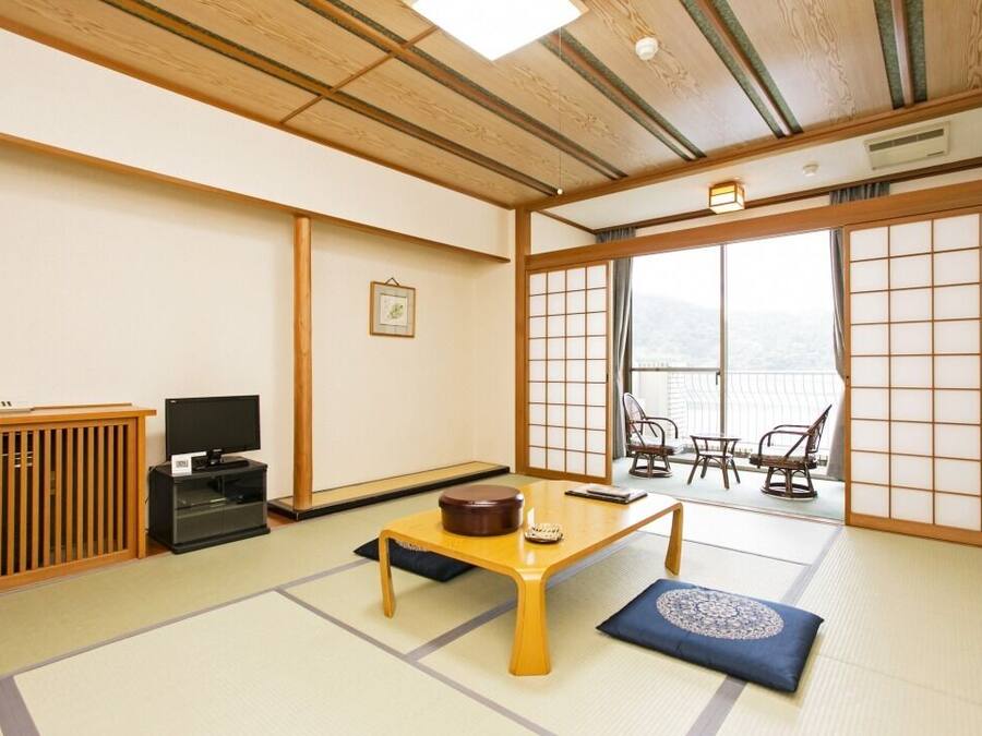 A traditional Japanese room with tatami flooring, a low wooden table, a television, and a sliding door leading to a balcony.