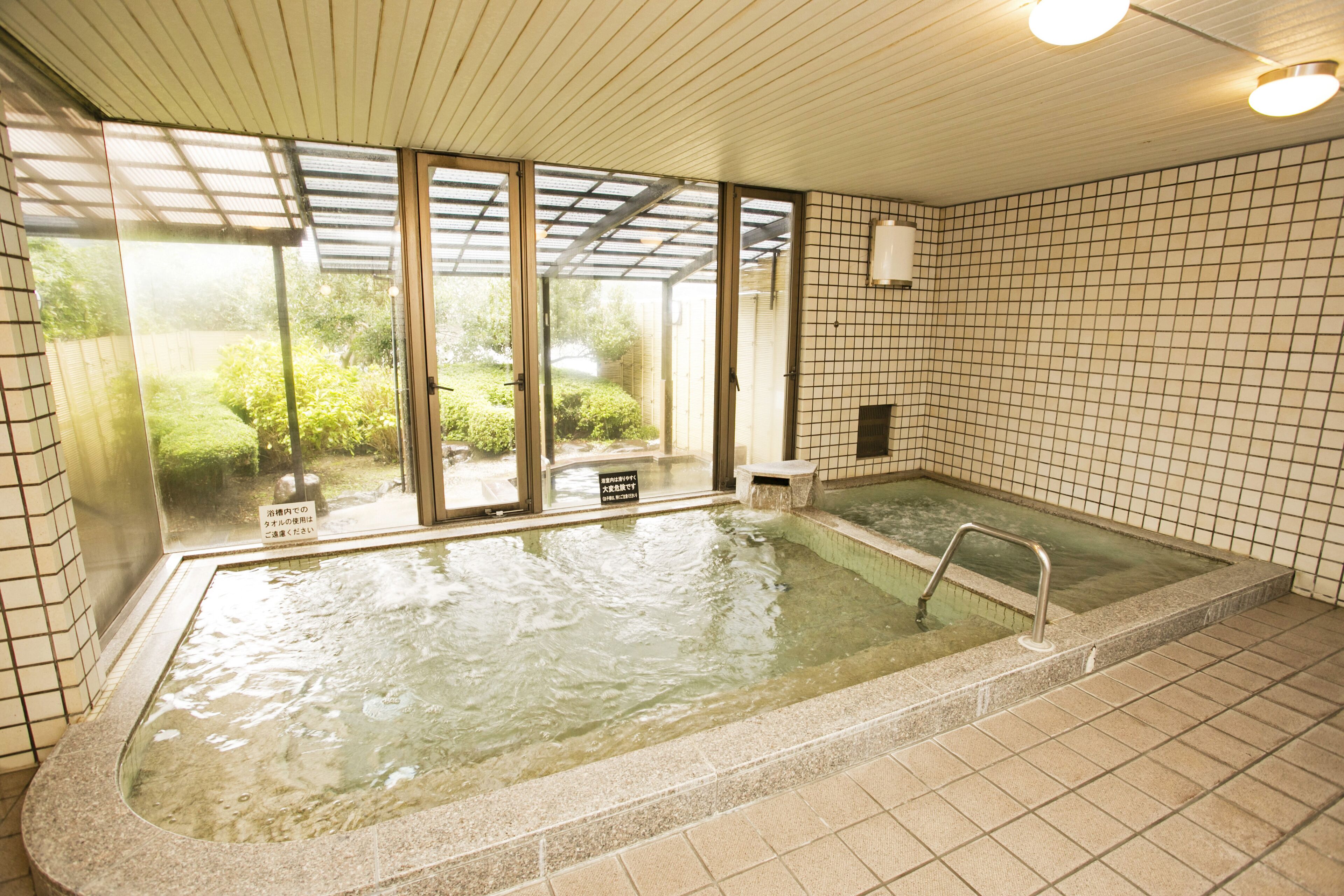 Ein Whirlpool mit Blick auf einen Garten, eine geflieste Wand und eine Decke mit Einbaustrahlern.