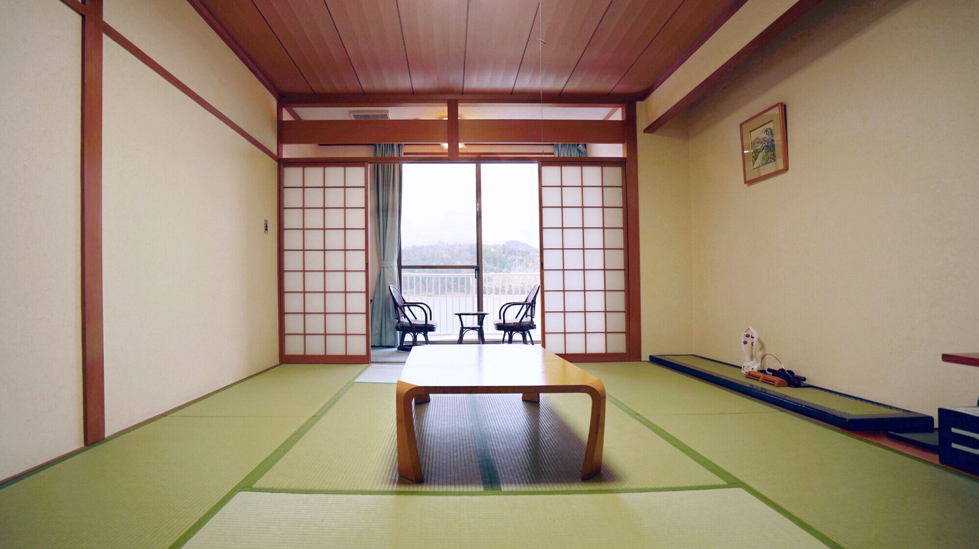 A tatami mat room with a low table and chairs, sliding doors, and a view of the outdoors.