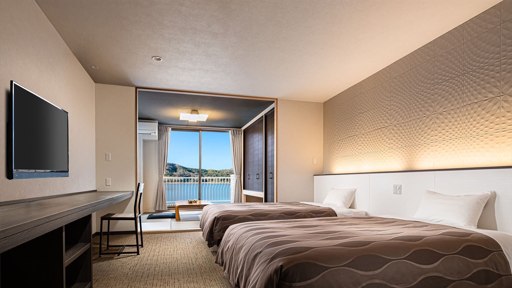 A hotel room with a TV, two beds, a desk, and a balcony with a view.