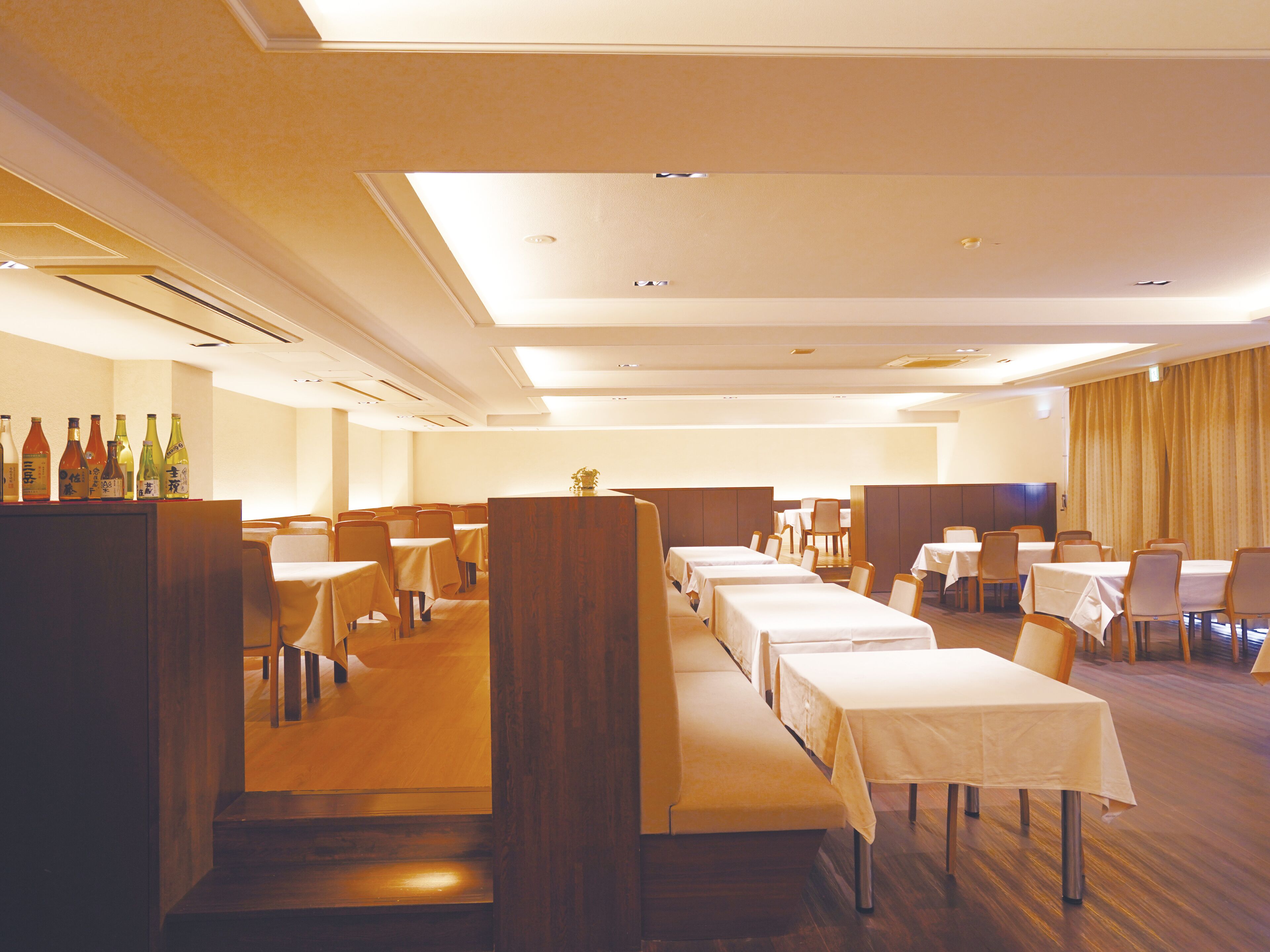 A hotel dining area with multiple tables and booths, a wooden reception desk, and a variety of bottles on display.