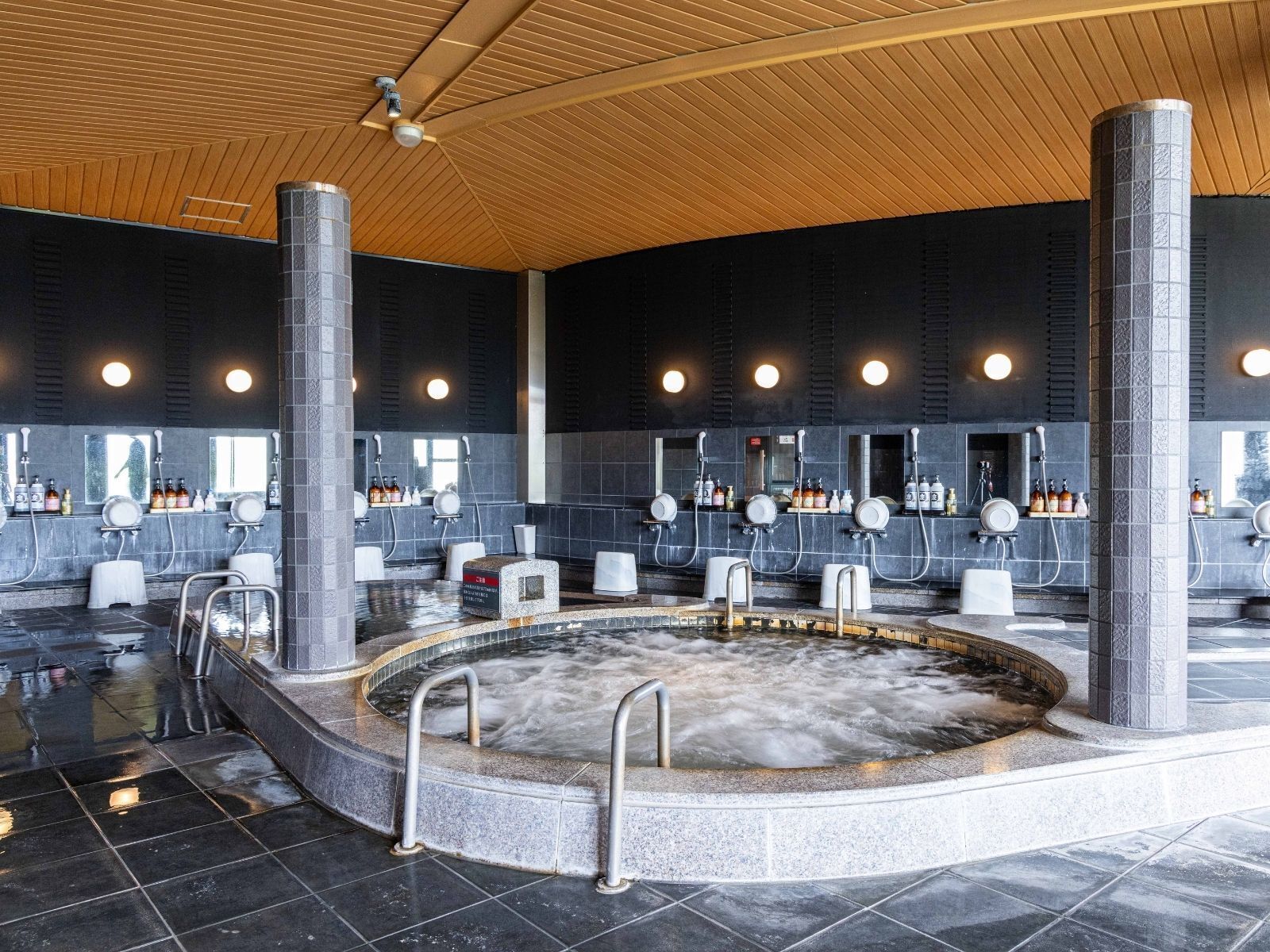 Een wellnessruimte met een jacuzzi, meerdere wastafels en een houten plafond.