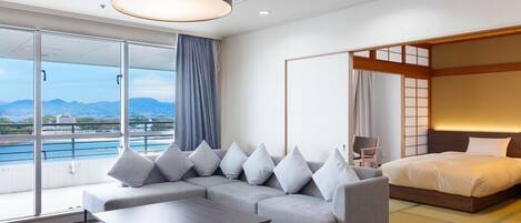 A modern hotel room with a sofa, a bed, a view of a cityscape, and a large window.