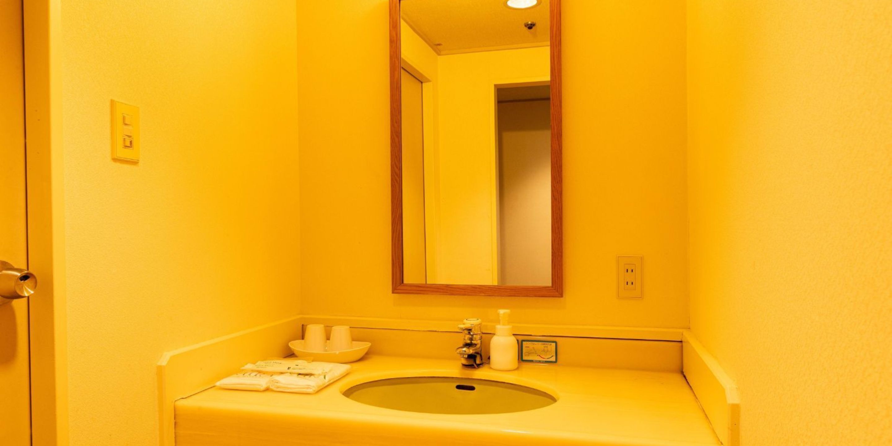 Een badkamer met een geel wastafel, een spiegel en een handdoekhouder.