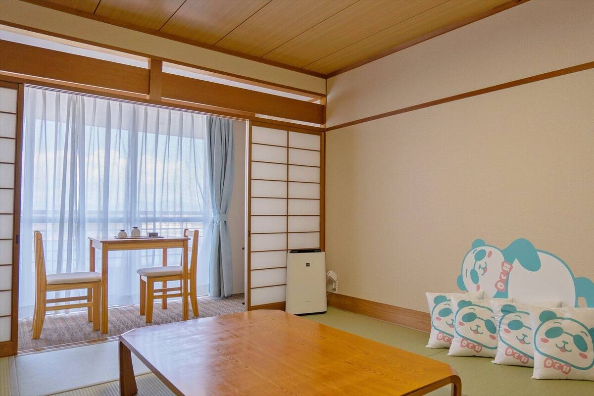 Una habitación japonesa tradicional con suelo de tatami, una mesa baja, un sofá y puertas correderas shoji.